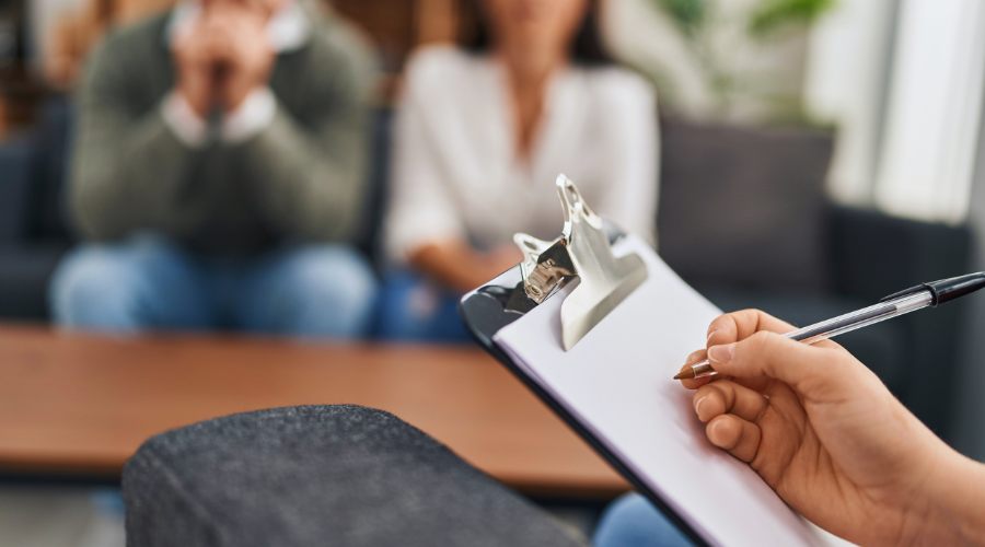 Insurance coverage for couples therapy concept pic shows therapist clipboard with couple in background